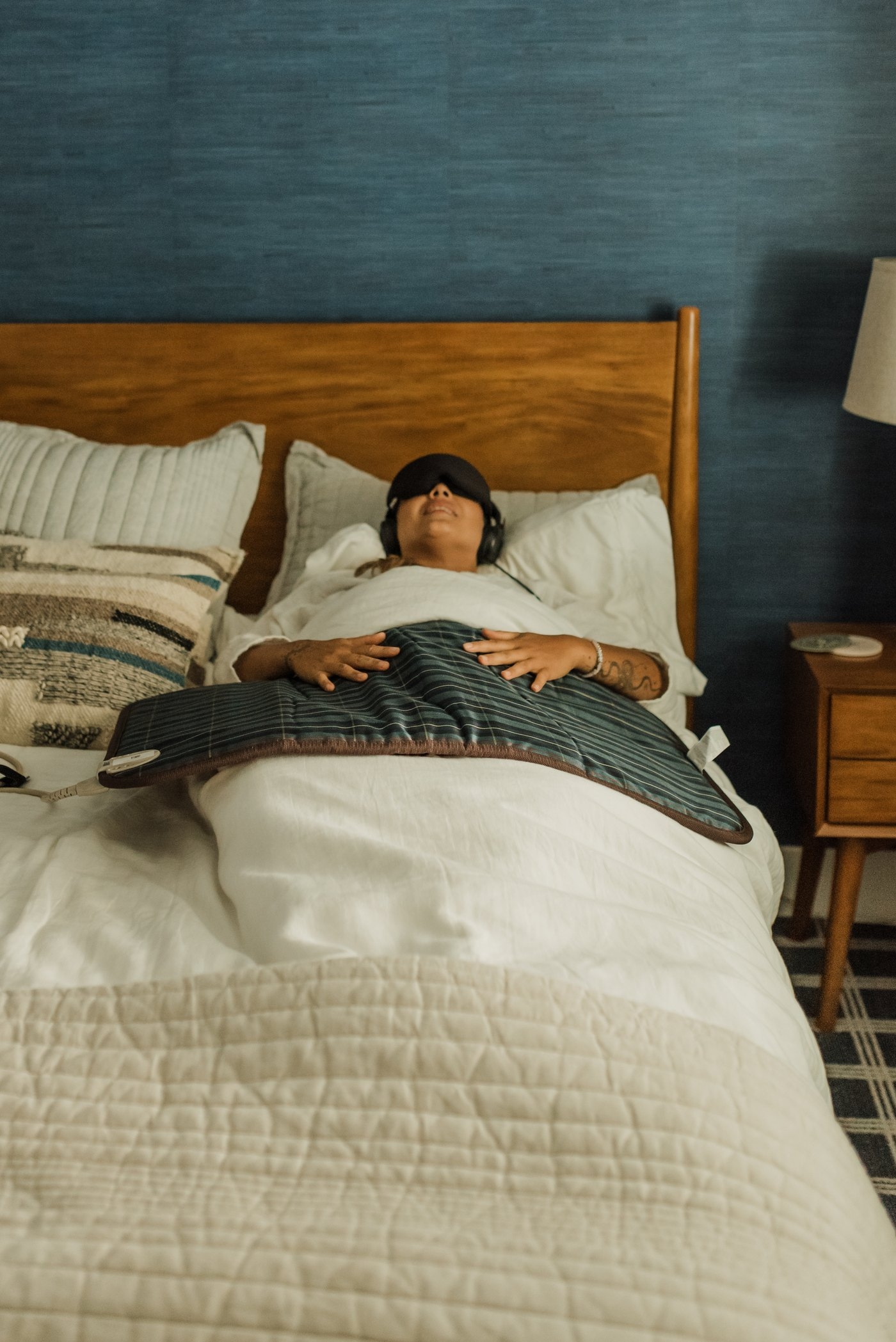 Woman resting in bed with the BioMat Mini laid across her, eye mask and headphones on
