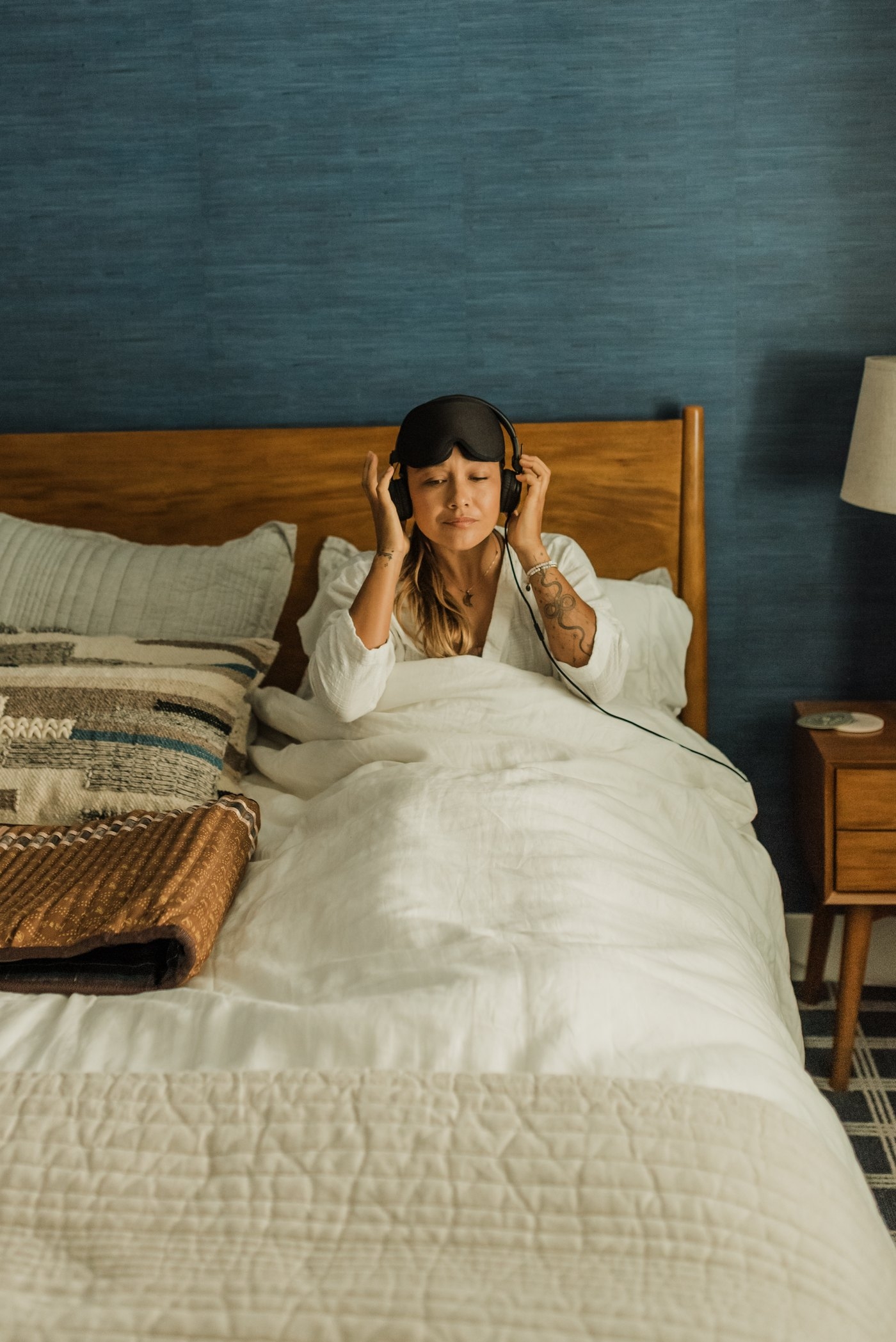 Woman in bed putting on headphones and an eye mask, her BioMat folded beside her