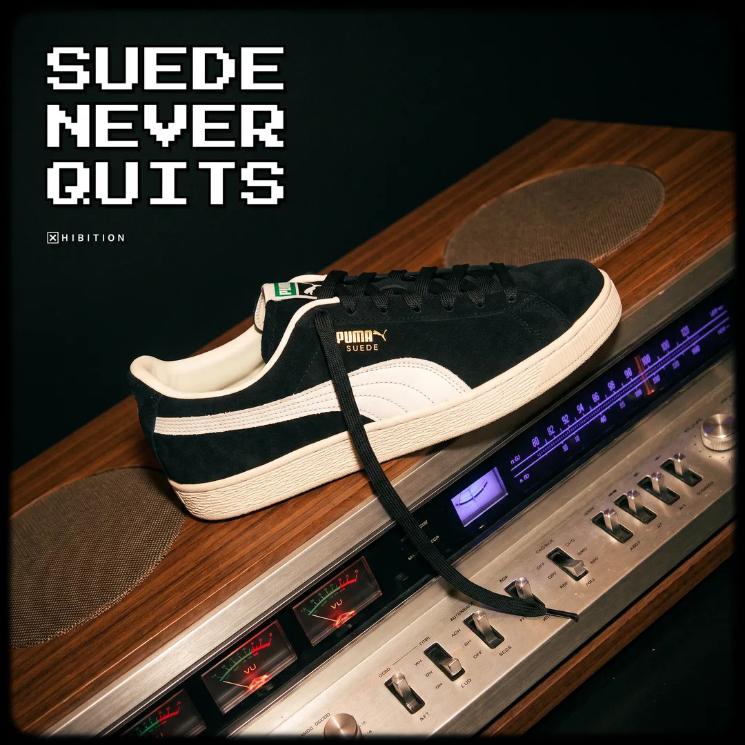 The PUMA Suede Charles F. Stead I in black suede with a single white curved formstrip and cream foxing sole, resting on a wood-panelled vintage hi-fi receiver. The campaign lockup reads Suede Never Quits above the Xhibition mark.
